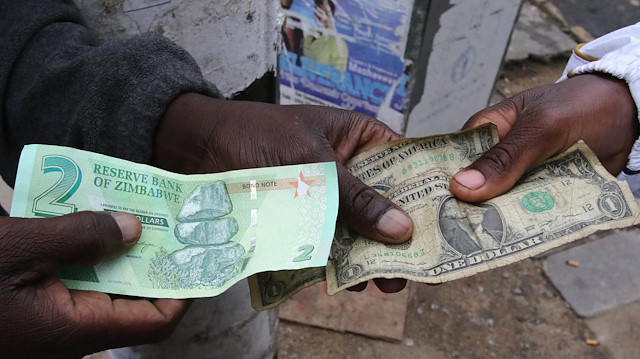 Illegal money changers pose while exchanging a new Zimbabwe bond note (L) and U.S. dollar notes in the capital Harare, Zimbabwe.