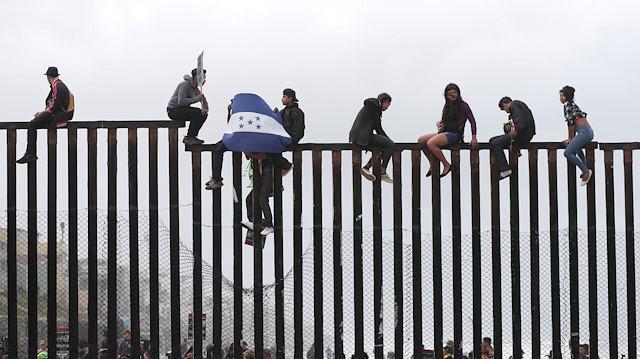 Members of a migrant caravan from Central America and their supporters sit on the top of the U.S.-Mexico border wall at Border Field State Park before making an asylum request, in San Diego, California, US
