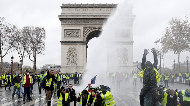 Protesters wearing yellow vests, a symbol of a French drivers' protest against higher diesel taxes, stand up in front of a police water canon at the Place de l'Etoile near the Arc de Triomphe in Paris, France.