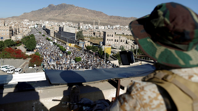 A Houthi militant sits guard on the roof of a building overlooking fellow Houthis rallying to denounce the rapid devaluation of the Yemeni Rial in Sanaa, Yemen October 5, 2018. 