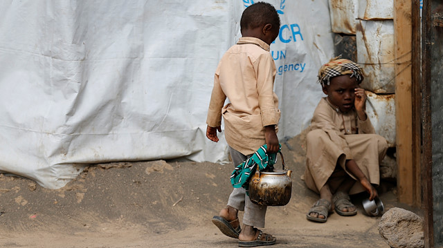 A boy holds a kettle as he walks outside his family's hut at a camp for people displaced by conflict