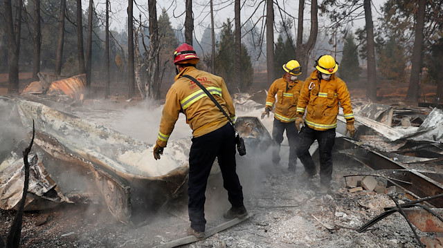 Firefighters move debris while recovering human remains from a trailer home destroyed by the Camp Fire in Paradise, California, US.