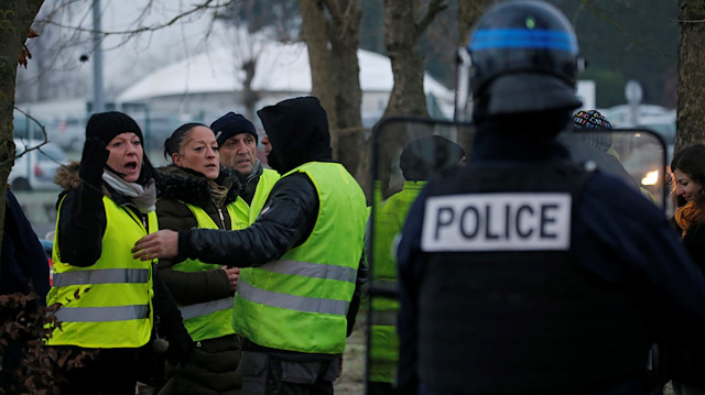 A protester wearing yellow vest reacts with French police as their shelter at a traffic island 