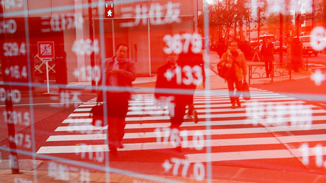 Pedestrians are reflected on an electronic board showing stock prices outside a brokerage in Tokyo, Japan.