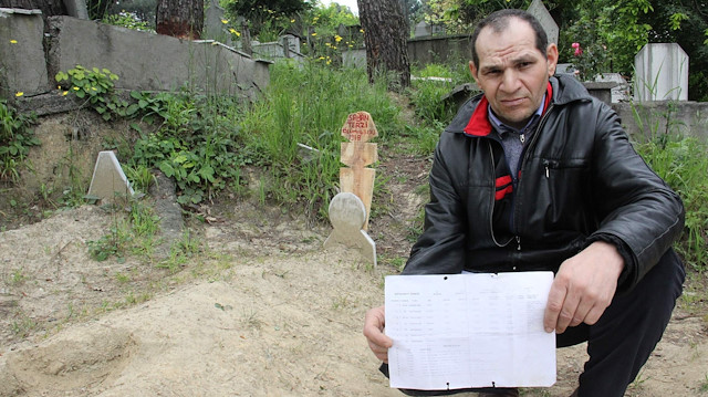 Bayram Ceran, ailesinin nüfus kayıt örneği ile babasının mezarı önünde.