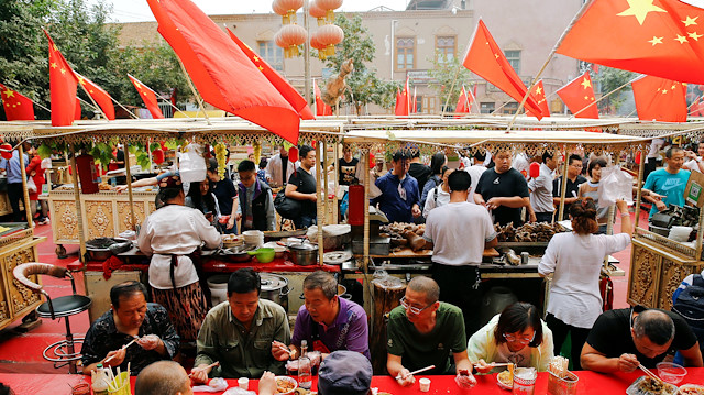 People eat under Chinese national flags in the Old City in Kashgar in Xinjiang Uighur Autonomous Region, China September 6, 2018. Picture taken September 6, 2018. To match Special Report MUSLIMS-CAMPS/CHINA REUTERS/Thomas Peter  