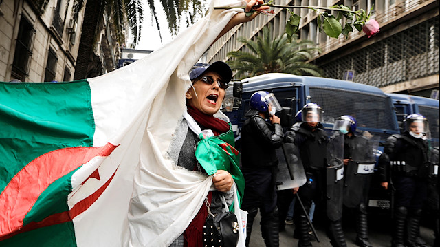 Police members stand guard as a woman carries a flower and a national flag during a protest 
