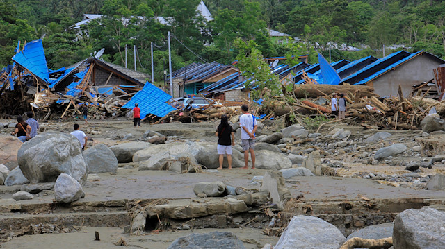 People stand as they look at damaged houses after a flash flood in Sentani, Papua, Indonesia