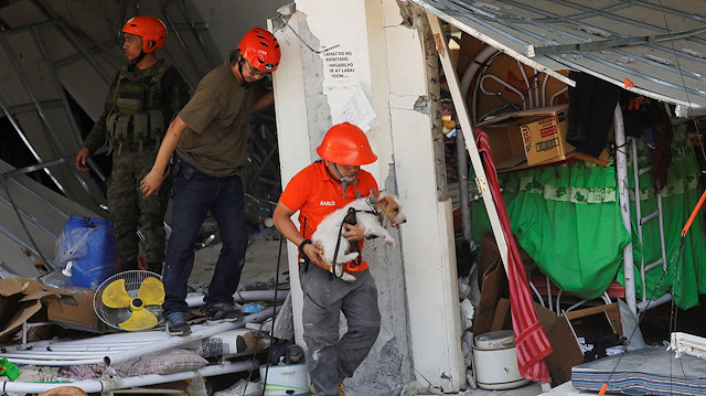 A rescuer carries a search dog as they try to reach survivors at a collapsed four-storey building following an earthquake in Porac town, Pampanga province, Philippines, April 23, 2019. 