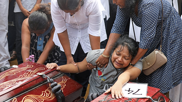 A woman reacts next to two coffins during a mass burial of victims