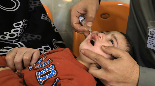 A boy receives polio vaccine drops by anti-polio vaccination workers 