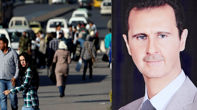 FILE PHOTO: A woman walks near a picture of Syrian President Bashar al Assad in Damascus, Syria April 15, 2018. REUTERS/Ali Hashisho/File Photo

