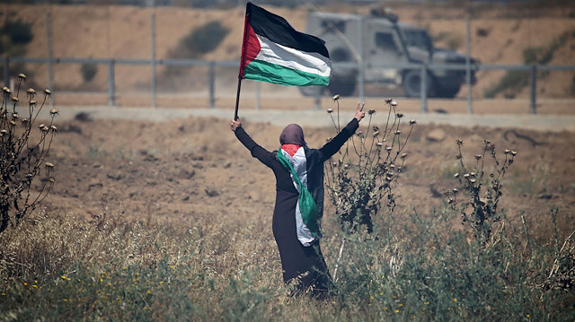 FILE PHOTO: A woman holding a Palestinian flag gestures in front of Israeli forces during a protest marking the 71st anniversary of the 'Nakba', or catastrophe, when hundreds of thousands fled or were forced from their homes in the war surrounding Israel's independence in 1948, at the Israel-Gaza border fence, in the southern Gaza Strip May 15, 2019. REUTERS/Ibraheem Abu Mustafa/File Photo  