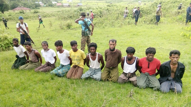 Ten Rohingya men with their hands bound kneel 