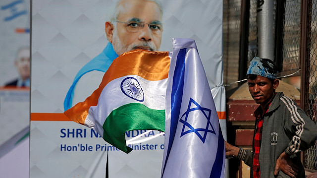 A man holds flags of India and Israel before installing them on a lamp post 