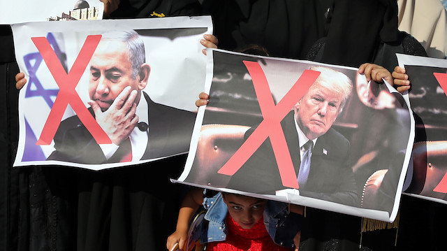 A girl looks on as Palestinian women hold crossed-out posters depicting U.S. President Donald Trump and Israeli Prime Minister Benjamin Netanyahu during a protest against Bahrain's workshop for U.S. peace plan, in the southern Gaza Strip, June 18, 2019. Picture taken June 18, 2019. REUTERS/Ibraheem Abu Mustafa

