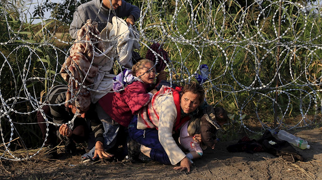 Syrian migrants cross under a fence as they enter Hungary