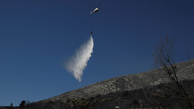 A firefighting helicopter makes a water drop during a wildfire on Mount Hymettus, near Athens