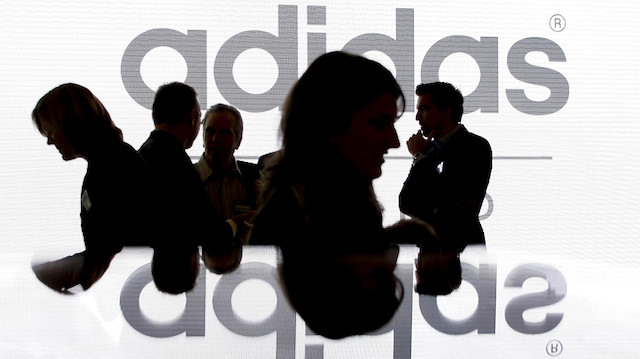 Shareholders of Adidas Group are silhouetted in front of the company logo.