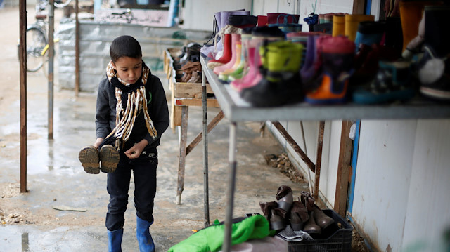 A Syrian child buys winter boots during rainy weather at the Al Zaatari refugee camp
