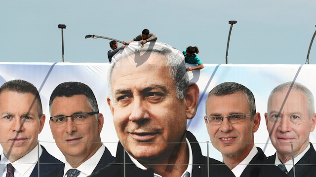 Labourers work on hanging up a Likud election campaign banner 