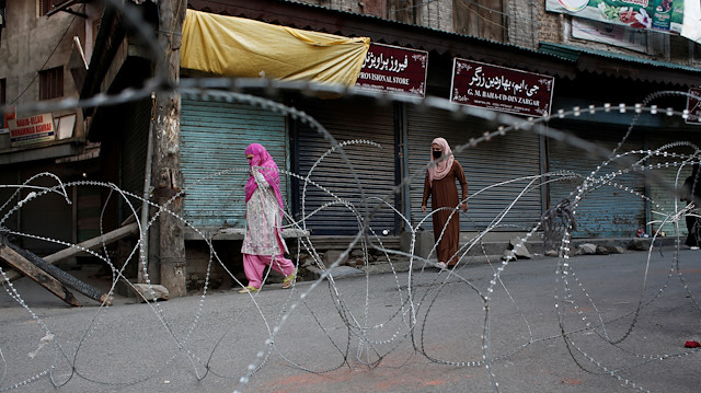 Fil photo: Kashmiri women walk past concertina wire laid across a road during restrictions