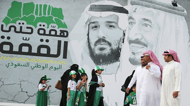 Saudi people walk past a poster depicting Saudi Arabia's King Salman bin Abdulaziz and Crown Prince of Saudi Arabia Mohammad bin Salman during the 89th annual National Day of Saudi Arabia in Riyadh, Saudi Arabia September 23, 2019. REUTERS/Ahmed Yosri 