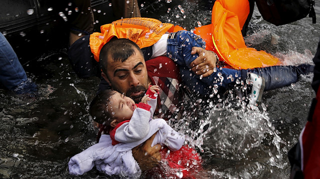 A Syrian refugee holds onto his children as he struggles to walk off a dinghy