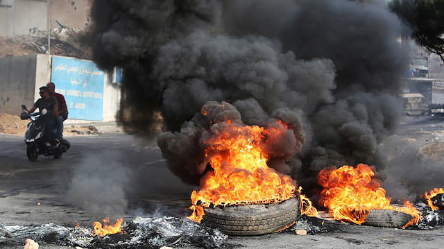 Men ride a motorbike past burning tires blocking a street during a protest targeting the government over an economic crisis, in Nabatiyeh, southern Lebanon 