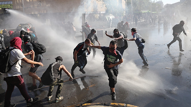 Demonstrators run as a riot police water cannon sprays water during a protest against Chile's state economic model in Santiago, Chile, October 21, 2019.