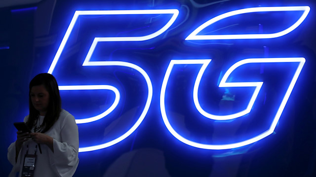 A woman looks at her mobile phone next to a 5G sign