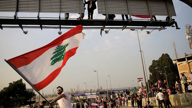 A protester waves a Lebanese flag as another one stands on a road sign at a demonstration blocking the highway during ongoing anti-government protests in Hazmiyeh, Lebanon November 13, 2019. REUTERS/Andres Martinez Casares