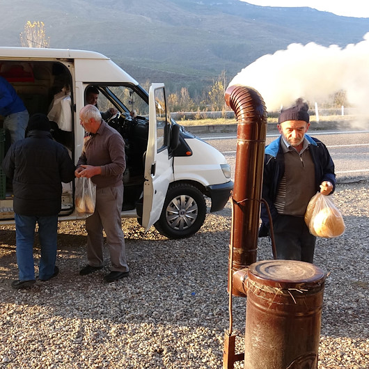Ekmek almak için bekledikleri durakta seyyar soba ile ısınıyorlar