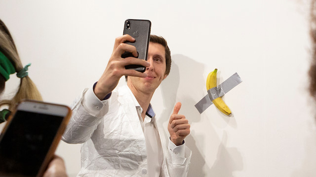 A man poses for a photo next to a banana attached with duct-tape 