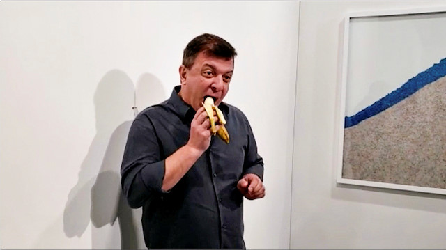 David Datuna eats a banana that was attached with duct tape to a wall, which was an artwork titled 'Comedian' by the artist Maurizio Cattelan, in front of a crowd at Art Basel in Miami Beach, Florida, U.S., December 7, 2019, in this still image from video obtained via social media.