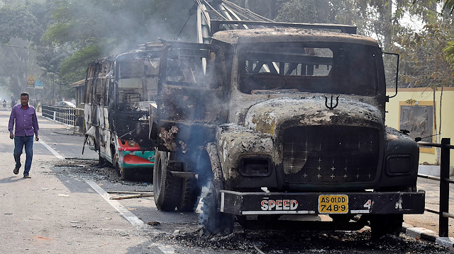 A man walks past damaged vehicles that were set on fire by demonstrators, during a protest after India's parliament passed Citizenship Amendment Bill, in Guwahati