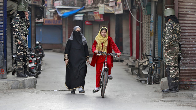FILE PHOTO: A Kashmir girl rides her bike past Indian security force personnel standing guard in front closed shops in a street in Srinagar, October 30, 2019. REUTERS/Danish Ismail/File Photo

