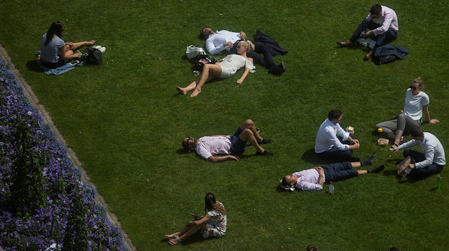 eople sit on a green during a lunch break in London, Britai