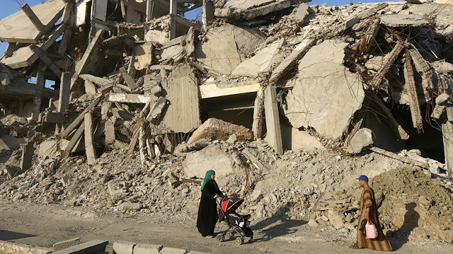 FILE PHOTO: A woman pushes a baby cart as she walks past rubble of damaged buildings in Raqqa, Syria, May 29, 2019. Picture taken May 29, 2019. 