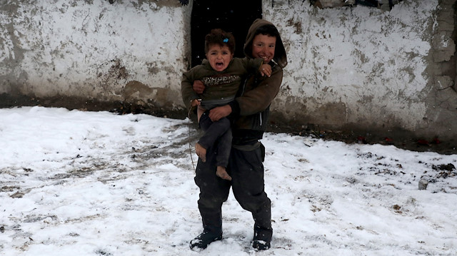 Internally displaced Afghan boys stands at the door of his shelter during a snowfall in Kabul