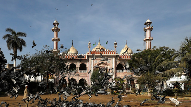 A man stands amid a swarm of pigeons as he is feeding them in front of a mosque in Karachi,