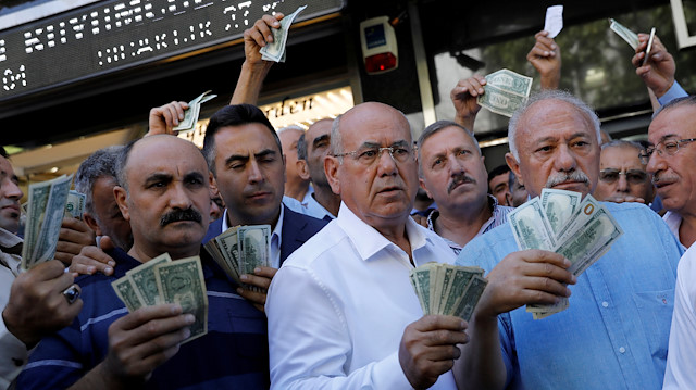 FILE PHOTO: Businessmen holding U.S. dollars stand in front of a currency exchange office in response to the call of Turkish President Tayyip Erdogan on Turks to sell their dollar and euro savings to support the lira, in Ankara, Turkey August 14, 2018. REUTERS/Umit Bektas/File Photo

