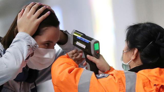 FILE PHOTO: A worker checks the temperature of a passenger arriving into Hong Kong International Airport with an infrared thermometer, following the coronavirus outbreak in Hong Kong, China, February 7, 2020