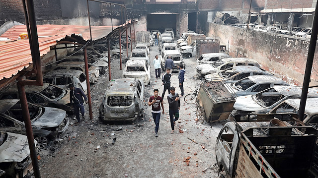 Men look at burnt vehicles at a parking lot in a riot affected area following clashes