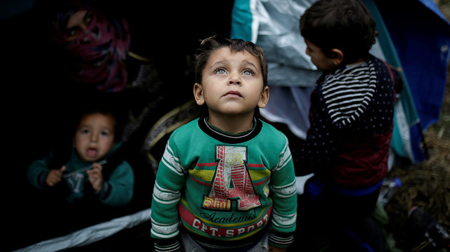 A Syrian refugee boy stands in front of his family tent at a makeshift camp