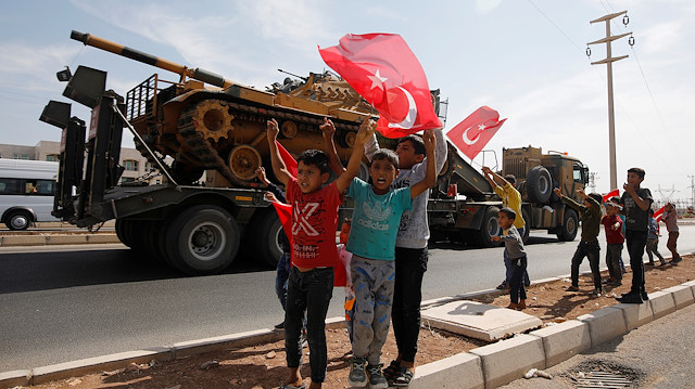 Boys wave Turkish flags as a military convoy 