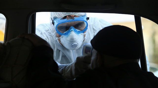 A member of the medical team checks the temperature of an old man in a car