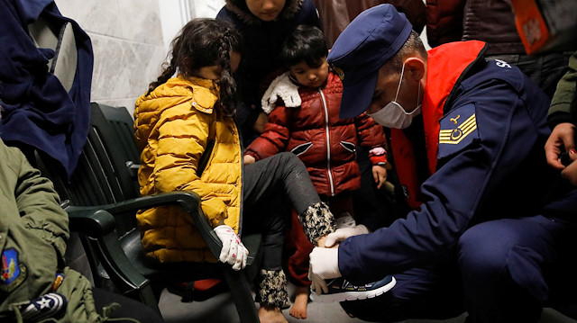 A Turiksh coast guard helps a girl put on a new pair of shoes as migrants wait to finish their registration formalities after they were brought to a coast guard station at the Turkish coastal town of Dikili, following a failed attempt to cross to the Greek island of Lesbos, in Balikesir province, Turkey, March 6, 2020.