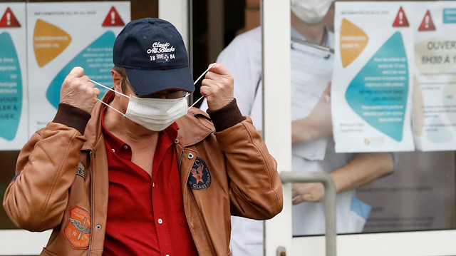 A man takes off a protective mask as he walks in front of placards 