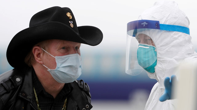 A worker in protective gear directs a masked passenger from a U.S. cruise ship